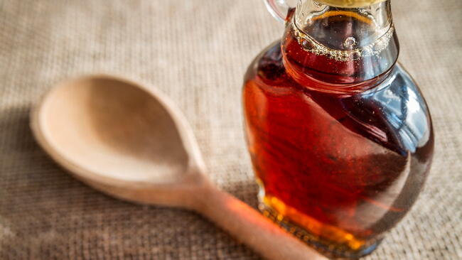 Glass bottle of maple syrup next to a wooden spoon